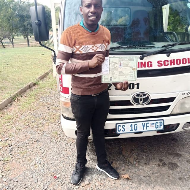 Tshepo T standing with a training vehicle and licence certificate after passing.